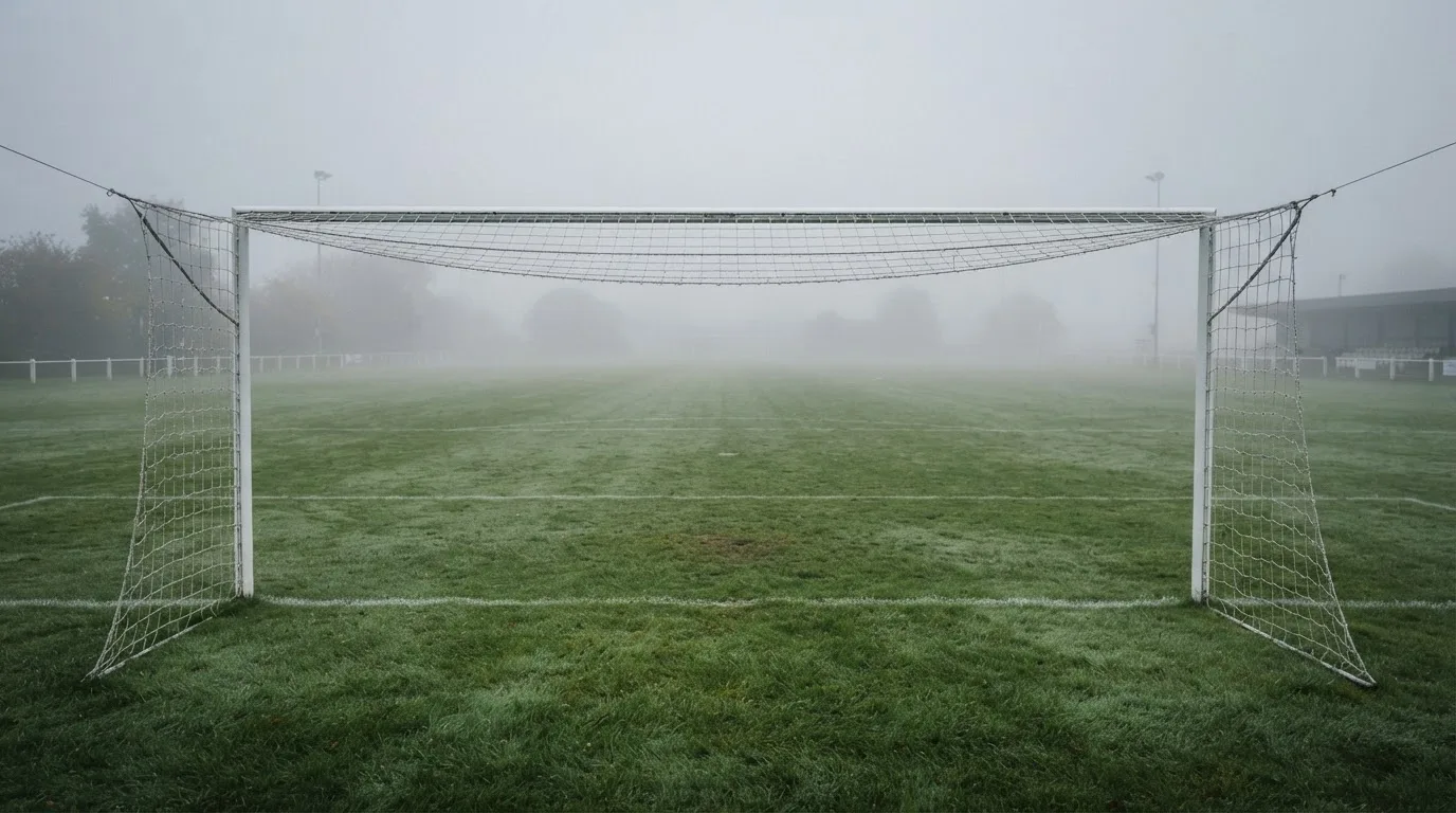 Ein leeres Fußballfeld im Morgennebel, die Mittellinie verliert sich im Dunst, kein Mensch ist zu sehen.