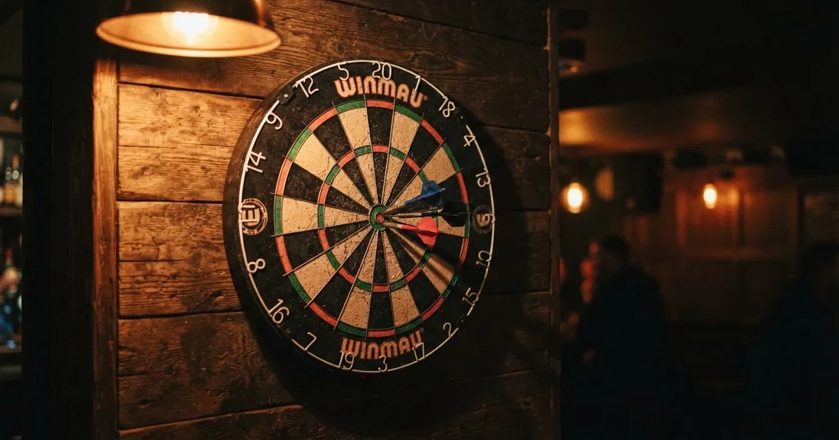 Eine Dartscheibe an einer Holzwand in einem schwach beleuchteten Raum, drei Pfeile stecken nahe der Mitte, warmes Licht von der Seite.