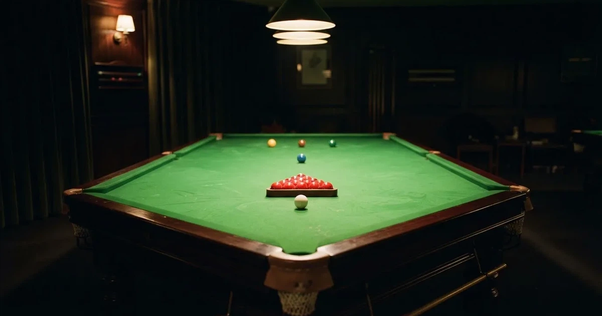 Ein Snookertisch mit grünem Tuch in einem abgedunkelten Saal, ein Lichtkegel fällt von oben auf die aufgestellten Kugeln.