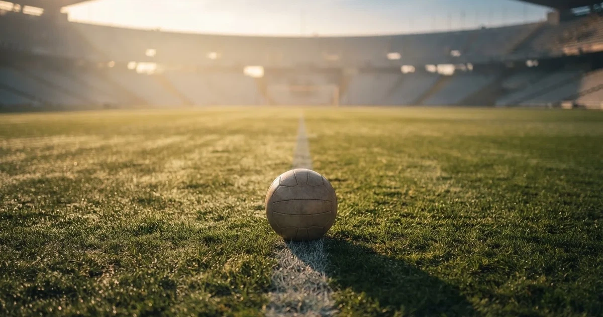 Ein Fußball liegt auf der Mittellinie eines leeren Rasenplatzes, die Kreidelinie verläuft scharf durchs Bild im Morgenlicht.